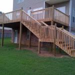 wood deck with set of steps leading down to a landing with another set of steps leading down to the concrete driveway